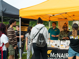 Photo of a yellow pop up tent with staff and students speaking to new students about campus resources