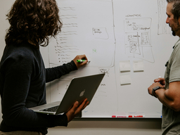 Picture of two people discussing and working with a white board.