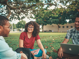 Three college students sitting on the grass talking.