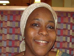 Ousseina Alidou is smiling towards the camera. She is seated in front of a patterned background.