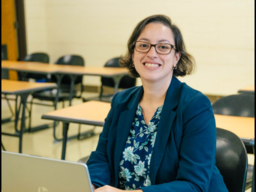 smiling woman sitting at classroom desk in front of laptop