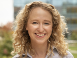 Smiling person with shoulder length curly blond hair and pinstripe shirt