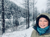 Dr. Skylar Bayer is smiling and standing in the snowy woods in Alaska.