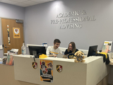 Two peer advisors sitting at the Office of Academic and Pre-Professional Advising front desk, they are reading
