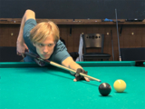 Josh leans over a pool table aiming pool cue at the cue ball.