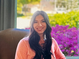Picture of Dr. Jackson Soller smiling, sat in a chair, with a background of green leaves, trees, a blurred house and purple flowers.